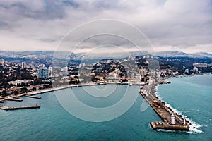 Aerial view of Yalta embankment from drone, old Lighthouse on pier, sea coast landscape and city buildings on mountains, Crimea