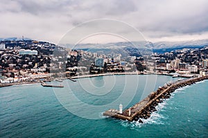 Aerial view of Yalta embankment from drone, old Lighthouse on pier, sea coast landscape and city buildings on mountains, Crimea
