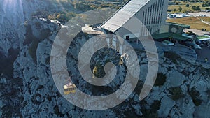 Aerial view of yellow elevator moving up on cable car near the high mountain slope covered by trees and shrubs. Shot