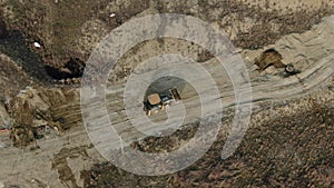Aerial view of a yellow tractor with a bucket full of soil which is excavating on a dirt road
