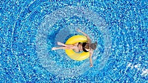 Aerial view of young brunette woman swimming on the inflatable big yellow in the pool. Top view of slim lady relaxing on her holid