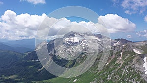 Aerial view of young couple on a mountain ridge against rocky cliffs, glacier and snowy peaks of Adygea. Amazing