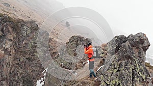 Aerial view of a young male photographer with a camera in his hands stands on a high rock in a gorge and photographs an