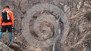 Aerial view of a young male photographer with a camera in his hands stands on a high rock in a gorge and photographs an