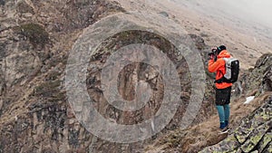 Aerial view of a young male photographer with a camera in his hands stands on a high rock in a gorge and photographs an