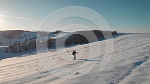 Aerial view young man hiking on top of snowy mountain at beautiful winter sunset. Male mountaineer with trekking poles