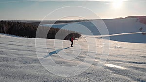 Aerial view young man hiking on top of snowy mountain at beautiful winter sunset. Male mountaineer with trekking poles