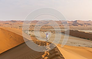 Aerial view of a young tourist with hands up on sand dunes in the Namib Desert, Namibia