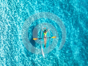 Aerial view of young woman lying on transparent canoe in blue se