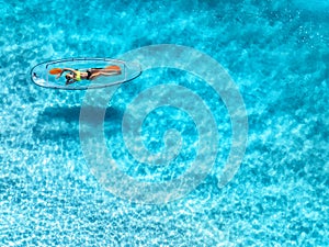 Aerial view of young woman lying on transparent canoe in blue se
