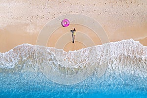 Aerial view of young woman with pink swim ring on the sandy beach