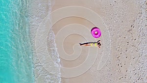 Aerial view of young woman with pink swim ring on the sandy beach