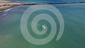 Aerial view of a young woman practicing stand up paddle surfing kneeling on the board