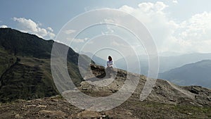 Aerial view of a young woman sitting on the top of epic cliff rock. Action. Concept of freedom and adventure, travelling