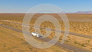 AERIAL: White freight truck hauls a cargo container across the barren landscape.