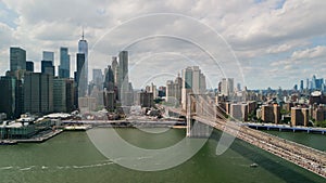 AERIAL wide shot over Brooklyn Bridge with American flag and East River view over Manhattan New York City Skyline