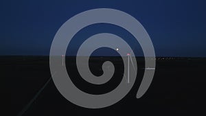 Aerial wide view of a close up wind turbine standing in a wheat field at night time.