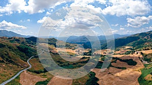 Aerial wide view panorama of fields and winding roads, farms, harvested grass, haystacks. Wind turbines in mountain, Passo Di
