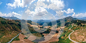Aerial wide view panorama of fields and winding roads, farms, harvested grass, haystacks. Wind turbines in mountain, Passo Di