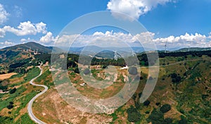 Aerial wide view panorama of fields and winding roads, farms, harvested grass, haystacks. Wind turbines in mountain, Passo Di