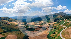 Aerial wide view panorama of fields and winding roads, farms, harvested grass, haystacks. Wind turbines in mountain, Passo Di