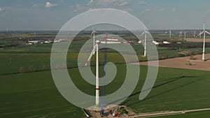 AERIAL: Wide View of Wind Turbine under construction being build on rich green agriculture field for renewable energy