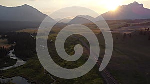 Aerial winding river with distant Canadian Rockies and train tracks at sunset