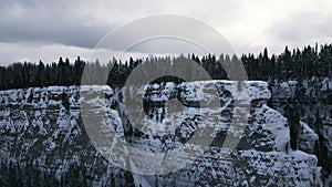 Aerial winter snow scene with ice covered cliff. Clip. White cliff edge with forested top.