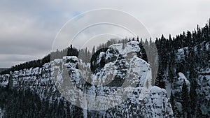 Aerial winter snow scene with ice covered cliff. Clip. White cliff edge with forested top.