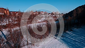 Aerial winter view high above rural village surrounded by pine tree forest.