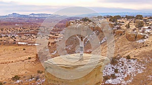 AERIAL: Woman raises her arms in victory while observing the canyon from boulder