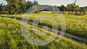 Aerial woman ride bike at green grass field. Summer nature landscape. Tourist girl drive bicycle