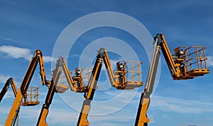 Aerial work platforms lined up against blue sky with clouds