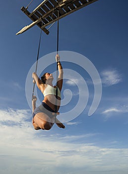 Aerial yoga beach workout - young attractive and healthy woman practicing aero-yoga training balance body and mind control hanging