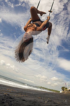 Aerial yoga beach workout - young attractive and healthy woman practicing aero-yoga training balance body and mind control hanging