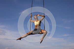 Aerial yoga beach workout - young attractive and healthy woman practicing aero-yoga training balance body and mind control hanging