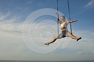 Aerial yoga beach workout - young attractive and healthy woman practicing aero-yoga training balance body and mind control hanging