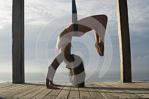 Silhouette of young attractive and healthy woman practicing aero-yoga training body balance hanging from ropes in front of the