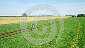 AERIAL: Young man cycling on bicycle at rural road through green and yellow field.