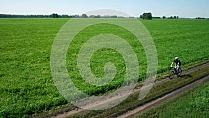 AERIAL: Young man cycling on bicycle at rural road through green and yellow field.