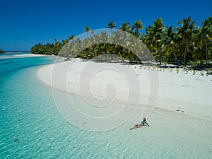 AERIAL: Young woman relaxing in the glassy ocean water by the lush exotic island