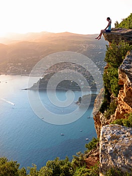 AERIAL: Young woman sitting on the edge of a cliff above the stunning seaside.