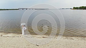 Aero, beautiful newlyweds standing on the beach, with glasses of champagne and under a transparent umbrella, against the