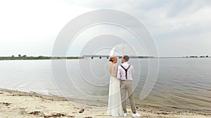 Aero, beautiful newlyweds standing on the beach, under a transparent umbrella, against the blue sky, river, and a large