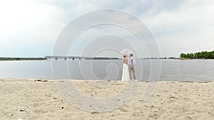 Aero, beautiful newlyweds standing on the beach, under a transparent umbrella, against the blue sky, river, and a large