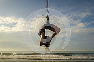 Aero yoga beach workout - silhouette of young attractive and athletic woman practicing aerial yoga exercise training acrobatic