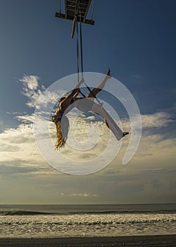 Aero yoga beach workout - silhouette of young attractive and athletic woman practicing aerial yoga exercise training acrobatic