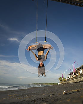Aero yoga beach workout - young attractive and athletic woman practicing aerial yoga exercise training acrobatic  body postures on