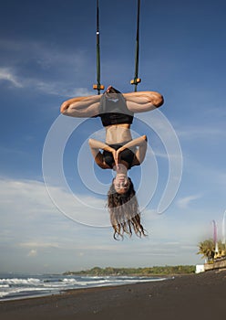 Aero yoga beach workout - young attractive and athletic woman practicing aerial yoga meditation exercise over the sea training