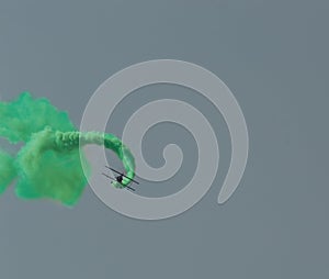 Aerobatic plane leaving a green smoke trail in the blue sky.